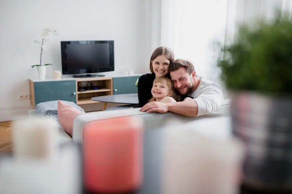 imagen de una familia de padre, madre e hija en el salon de casa mirando a cámara muy sonrientes